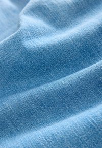 Tissu bleu clair doux avec texture de tissage visible et plis délicats créant des vagues et des ombres.