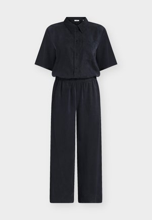 Melna īsroku krekla ar pogām priekšpusē un kabatu, kopā ar saskaņotām augsta vidukļa platām biksēm uz balta fona.