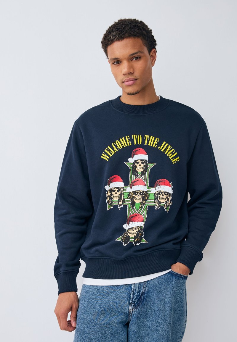 Mörkblå sweatshirt med en grafisk design med skallar i tomteluvor och texten "WELCOME TO THE JINGLE" i gult.