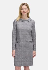 Vestito a quadri grigio con scollo a cascata, maniche lunghe, due tasche frontali con dettagli decorativi e una silhouette aderente.
