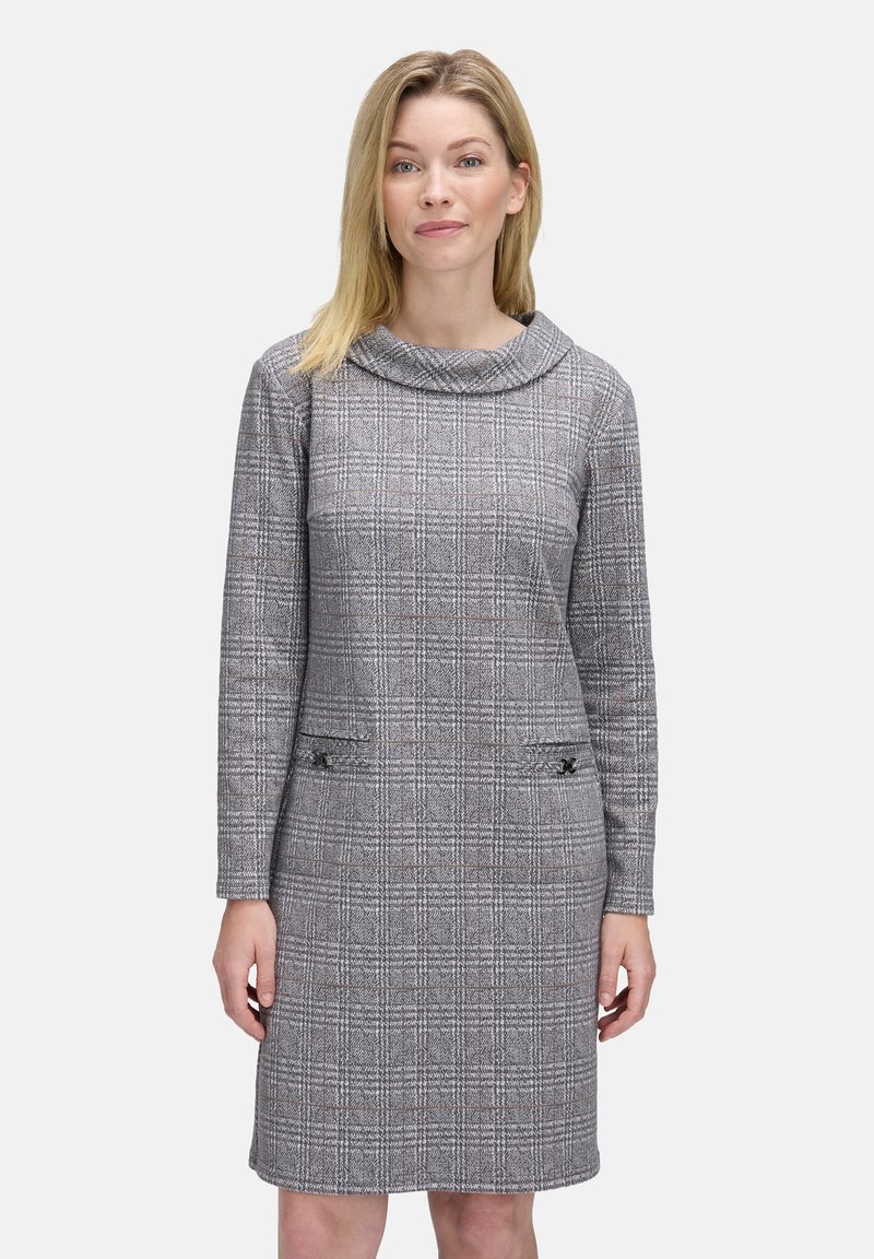 Vestito a quadri grigio con scollo a cascata, maniche lunghe, due tasche frontali con dettagli decorativi e una silhouette aderente.