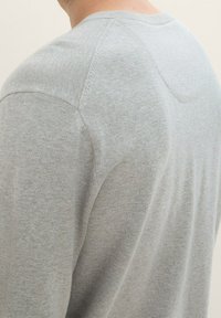 Chemise en coton grise à manches longues avec un col rond et des manches montées, présentant une texture lisse et des détails de couture minimaux.