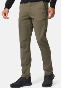 Chinos verde oliva con corte recto, fabricados en tejido suave; cuentan con bolsillos frontales y una cinturilla limpia, combinados con zapatillas negras.