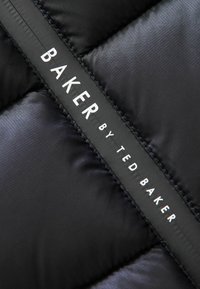Melnas puffa jakas materiāls ar izšūtu tekstūru. Izceļas izteikta melna birka ar baltu tekstu: "BAKER by TED BAKER."