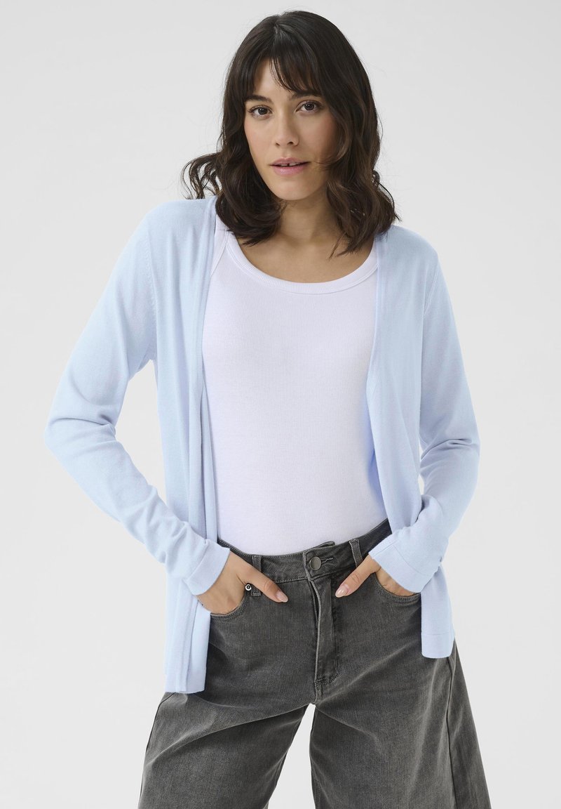Lichtblauwe cardigan gemaakt van een zachte, gestructureerde stof met lange mouwen en een open voorkant, gecombineerd met een wit topje en grijze high-waisted broek.