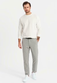 Ljusbeige långärmad skjorta, grå åtsittande byxor och vita sneakers. Slätt tyg, skräddarsydd passform och minimalistisk design. Inga mönster synliga.