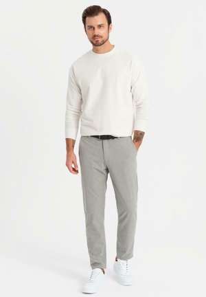 Lichtbeige lange mouw shirt, grijze fitted broek en witte sneakers. Glad stof, getailleerde pasvorm en minimalistisch design. Geen patronen zichtbaar.