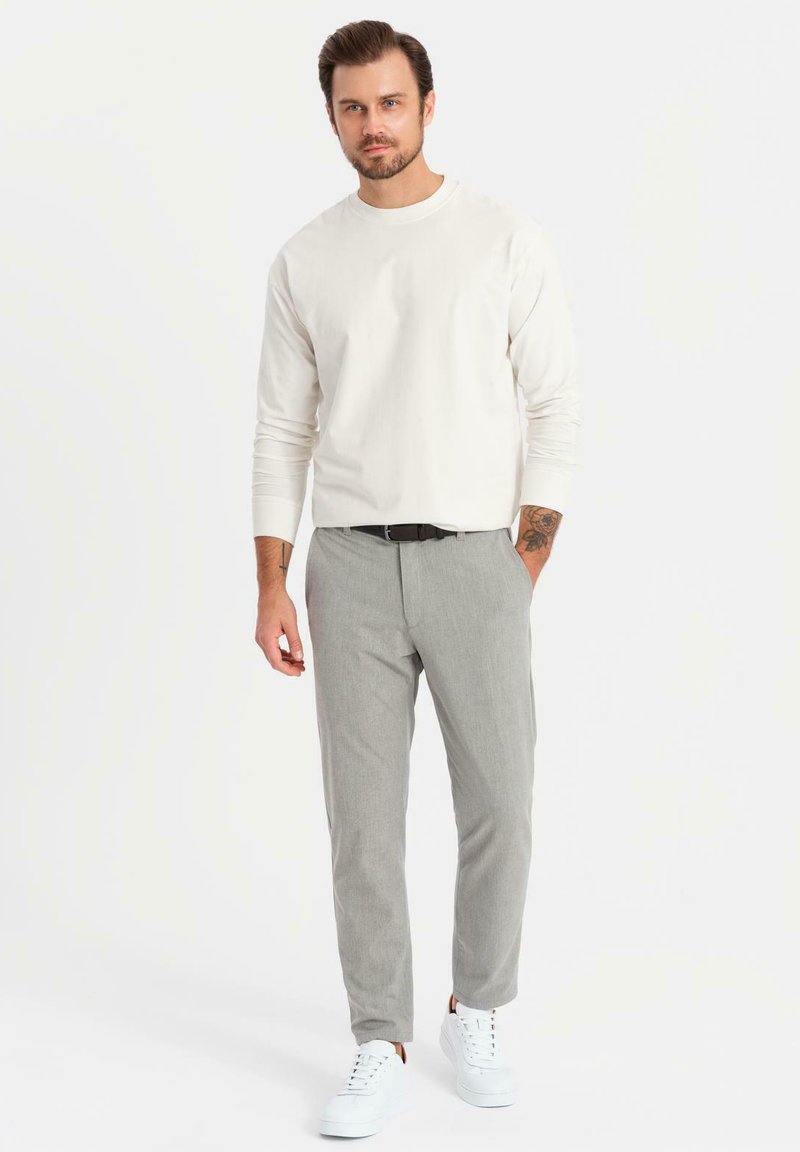 Ljusbeige långärmad skjorta, grå åtsittande byxor och vita sneakers. Slätt tyg, skräddarsydd passform och minimalistisk design. Inga mönster synliga.