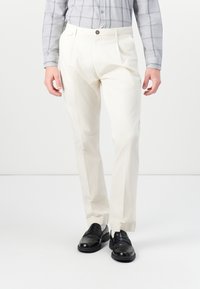 White, straight-leg trousers featuring subtle texture, front pleats, and a single button closure, paired with black loafers.