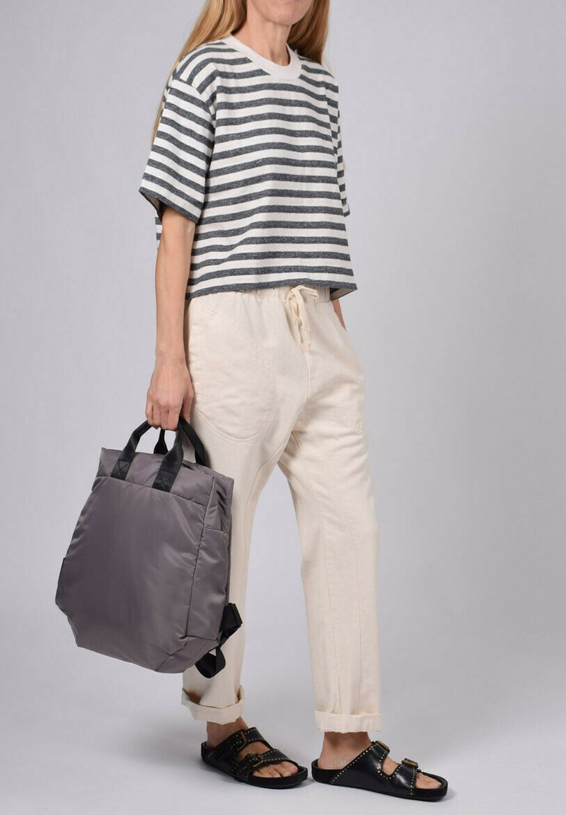 Camiseta corta a rayas gris y blanca, pantalones beiges con cordón, y una bolsa acolchada gris con asas negras. Sandalias negras con tachuelas.