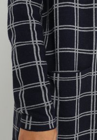 Marinblå stickad klänning med vitt rutmönster, långa ärmar och sidficka. Mjuk textur och avslappnad passform som passar för vardagsbruk.