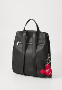 Zaino in pelle nera con due manici superiori, tasca frontale con zip e un portachiavi di Topolino rosso attaccato. Superficie texture con hardware minimal.