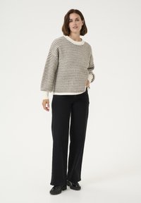Pulover tricotat gros cu un model în carouri alb și negru, guler și manșete crem, asortat cu pantaloni largi negri și pantofi negri.