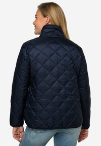 Marinblå vadderad pufferjacka med hög krage, som har ett diamantmönster, syntetiskt material och en slät yta.