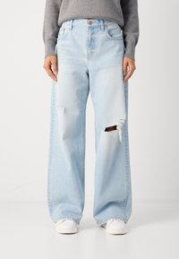 Jeans anchos de color azul claro, hechos de denim, con desgastes y roturas en las rodillas. Presentan un diseño clásico de cinco bolsillos y un cierre de botón.