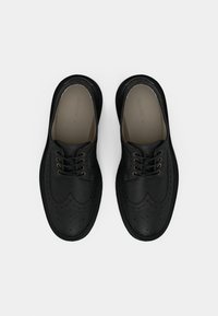 Chaussures en cuir noir avec un design brogue, bout rond, surface texturée et lacets marron. Présentent des perforations décoratives le long des bords.