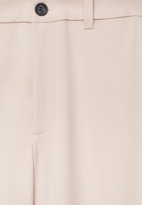 Pantalon beige en tissu lisse, coupe droite, poche avant et bouton noir à la taille. Design épuré et minimaliste.