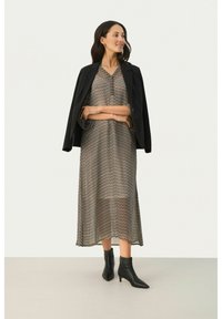 Blazer noir sur une robe maxi fluide et à motifs en créme et marron avec un design en chevrons, assortie à des bottines noires à talons pointus.