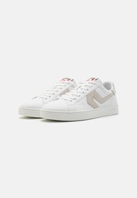 Białe sneakersy z gładką skórzaną cholewką, szarymi zamszowymi akcentami po bokach i teksturowaną gumową podeszwą. Posiadają okrągłe sznurówki i naszywkę z logo na języku.
