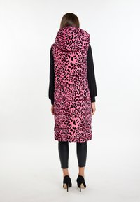 Vesta căptușită de culoare roz aprins cu pete negre de leopard, având o glugă mare și buzunare laterale, combinată cu pantaloni negru ajustați și pantofi cu toc.