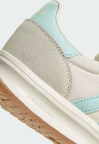 Teniska s vrškom zo svetlosivej semišovej kože so svetlozelenými detailmi, bielou medzipodrážkou a textúrovanou gumovou podrážkou označenou ako "CLOUDFOAM".