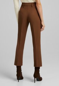 Bruna skräddarsydda byxor med rak benpassform, hög midja och subtil vertikal sömnad, i kombination med bruna klackade ankelskor.