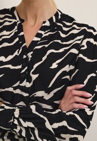 Blouse à imprimé zèbre noir et crème avec un col, des boutons et des poignets plissés. Le matériau semble léger et texturé.