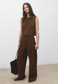 Hnědý top bez rukávů a široké kalhoty z texturovaného materiálu, doplněné černou kabelkou a elegantními černými botami.