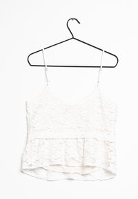 Top de peplum de encaje blanco en un perchero negro, con tirantes delgados ajustables, un patrón floral texturizado y un forro interior suave.