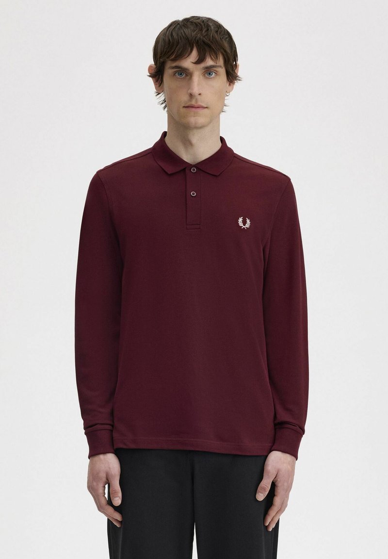 Polo a maniche lunghe in cotone bordeaux, con colletto, pattina con tre bottoni e un piccolo emblema bianco sul lato sinistro del petto.