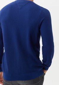 Blå ribbad tröja med en V-formad söm på baksidan, långa ärmar och en åtsittande midja, tillverkad av ett strukturerat stickat tyg.