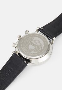Montre chronographe avec un boîtier en acier inoxydable et un bracelet en cuir noir. Design de globe gravé au dos, avec une quincaillerie en acier argenté.