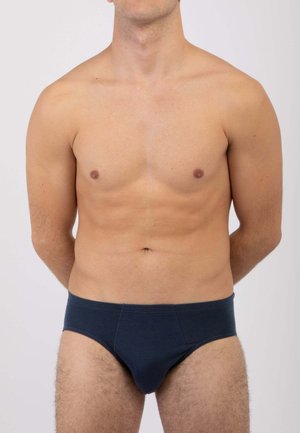 Slip in cotone blu navy con fascia elastica in vita, che mostrano una texture liscia e una forma aderente, indossati da un modello maschile a torso nudo.