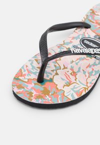 Chinelo de plástico preto com uma alça texturizada, apresentando um padrão floral multicolorido em uma palmilha de espuma, sola cinza.