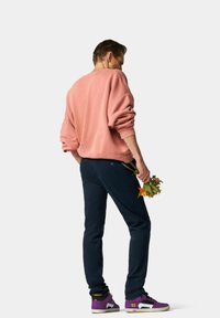 Un sweat-shirt surdimensionné rose clair, un pantalon bleu marine et des baskets violettes. La personne tient un petit bouquet de fleurs dans une main.