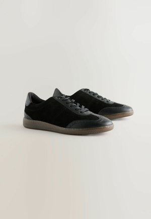 Black sneakers with suede and leather material, low-top design, textured accents, round toe, and rubber sole with a patterned tread.