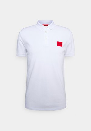 Polo blanc à manches courtes avec col, trois boutons et un patch rectangulaire rouge avec texte noir sur la poitrine gauche.