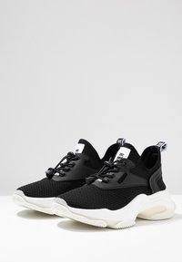 Baskets en tricot noir avec une semelle blanche épaisse, design à lacets, col rembourré, et accents de logo sur le talon et la languette.