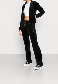 Black velour tracksuit with zip-up jacket and drawstring pants. Features blue logo accents and a fitted white crop top, paired with black sneakers.