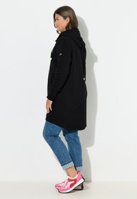 Vestido con capucha negro con textura, combinado con vaqueros azules remangados y vibrantes zapatillas rosas con suela blanca y detalles rojos.