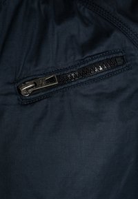 Close-up of a dark blue fabric with a black metal zipper partially closed, featuring visible stitching around the zipper area.