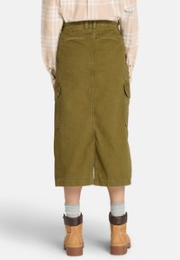 Falda cargo verde oliva con dos bolsillos laterales, de longitud hasta la rodilla y una abertura en la parte trasera. El material parece resistente y tiene una textura suave.