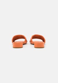 Orange open-back sandals with a woven strap design, featuring a low block heel and smooth texture for comfort and style.