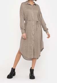 Brown and beige checked shirt dress with long sleeves, button front, and tie waist. Paired with black ankle boots. High-low hemline.