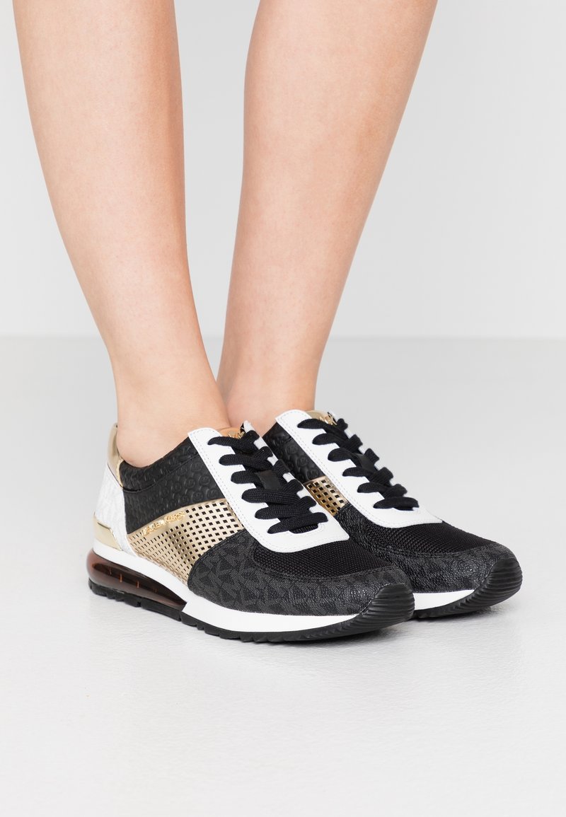 Black and white athletic shoes with gold accents; mesh and textured surfaces; black laces; rubber sole; designed for comfort and support.