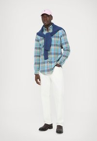 Rutete skjorte med knapper i blått og grønt, med en blå genser knyttet rundt halsen, hvite bukser og svarte sko. Rosa caps fullfører antrekket.