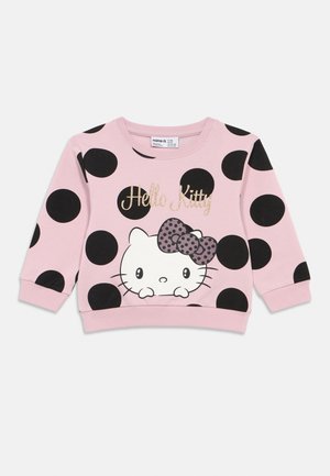 Pink sweatshirt with large black polka dots. Features a Hello Kitty graphic with a spotted bow. Ribbed cuffs and hem. Soft fabric texture.