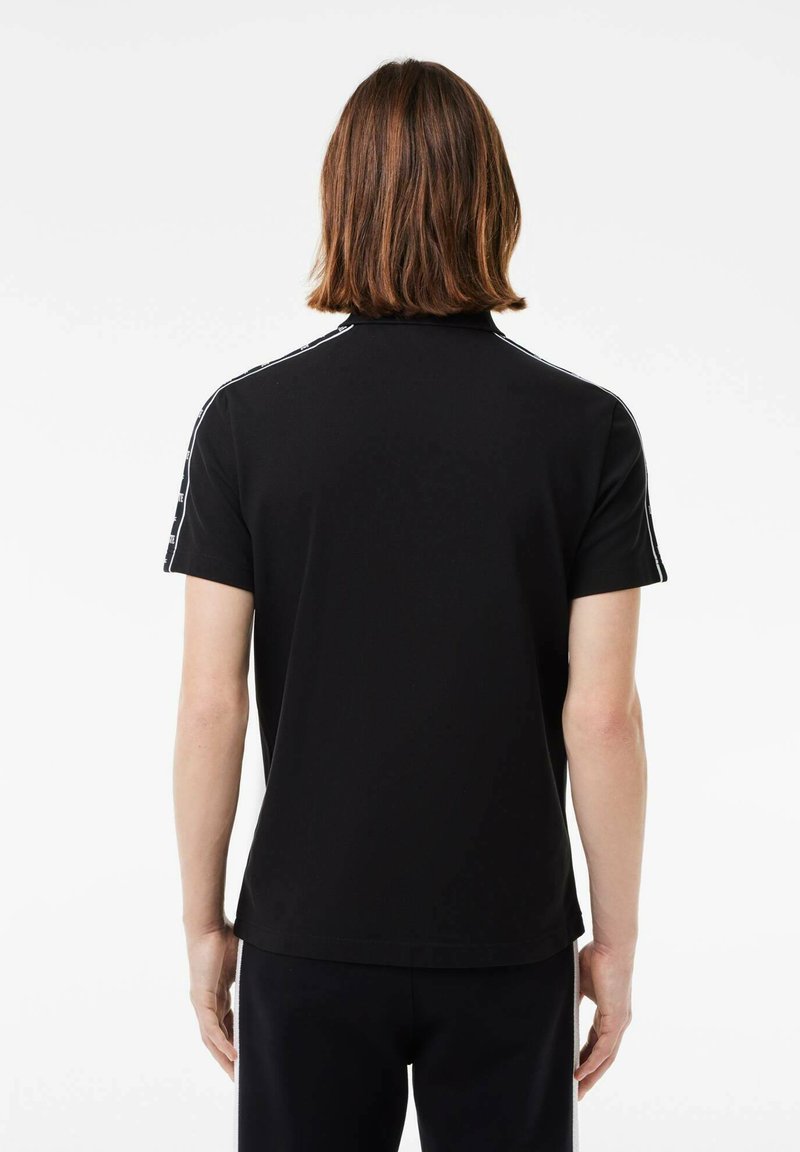 Camisa polo negra hecha de una tela suave, con mangas cortas y rayas blancas en los hombros. Diseño de cuello clásico.