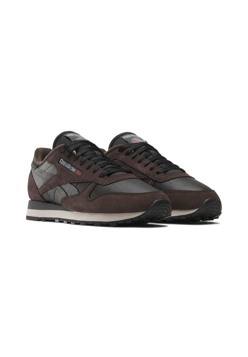 Baskets en daim marron et en cuir noir avec des lacets noirs, un col rembourré, une semelle en caoutchouc et un logo Reebok sur le côté et sur la languette.