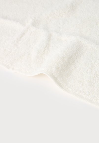 Tissu éponge blanc doux avec une surface moelleuse et texturée, légèrement plié sur un fond propre et lisse.